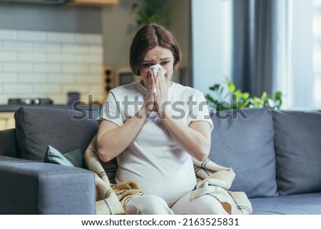Sad pregnant woman at home sitting on the couch and crying, has a runny nose and allergies sneezes into a napkin Royalty-Free Stock Photo #2163525831