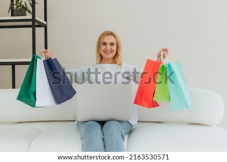 portrait happy mature woman hold shopping bags at home. Online shopping. Senior woman using laptop shopping online