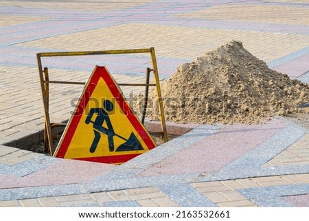 Road sign repair work on the pavement near a pit and a pile of sand