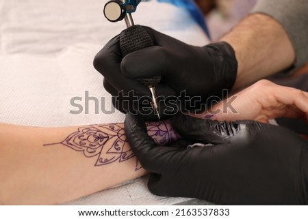 Professional artist making tattoo on hand at table, closeup