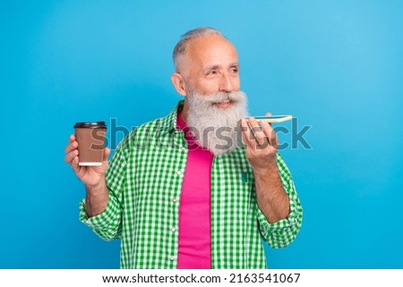 Photo of cheerful granddad hold coffee cup telephone record voice message isolated on blue color background
