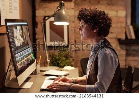 Young professional colorist sitting at her workplace in front of computer monitor and editing photos on special software
