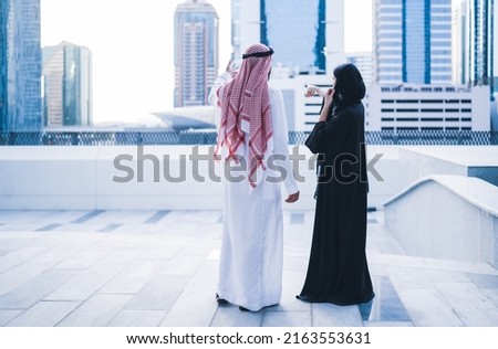 Back view of Arab family or business work colleagues pointing towards city skyline wearing traditional abaya and dress. Muslim Saudi or Emirati couple or team working together Royalty-Free Stock Photo #2163553631