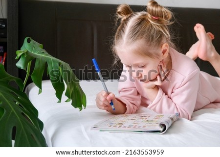 Portrait of a schoolgirl solves children crosswords on the bed. Logic games at home. solving crossword puzzles  Royalty-Free Stock Photo #2163553959