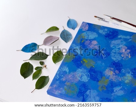 DIY Abstract botanical art. The picture is made by applying acrylic paints on the leaves and stamping on canvas. Blue on blue.