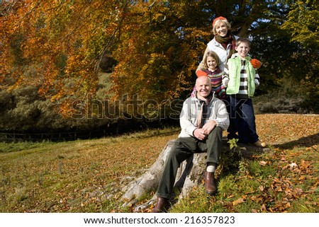 Portrait of grandparents and grandkids in field with autumn leaves