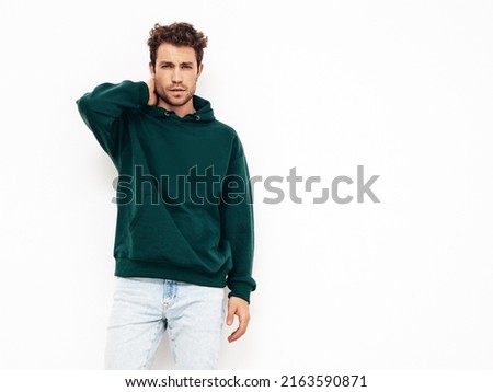 Handsome confident hipster  model.Sexy unshaven man dressed in summer stylish green hoodie and jeans clothes. Fashion male with curly hairstyle posing in studio. Isolated on white Royalty-Free Stock Photo #2163590871