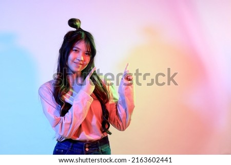 The cute young Asian girl with casual clothes posing under the gel color lightning in studio.