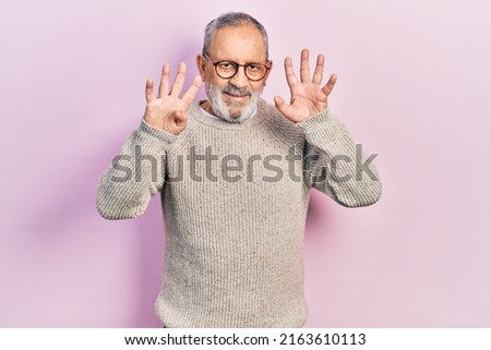 Handsome senior man with beard wearing casual sweater and glasses showing and pointing up with fingers number nine while smiling confident and happy. 