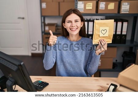 Young brunette woman working at small business ecommerce smiling happy and positive, thumb up doing excellent and approval sign 
