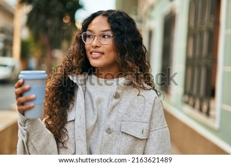 Young latin woman smiling happy drinking coffee at the city.