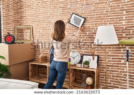 Young woman on back view hanging picture on wall at new home