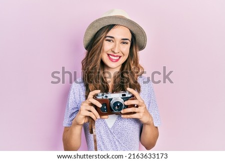 Young hispanic girl wearing summer hat holding vintage camera smiling with a happy and cool smile on face. showing teeth. 