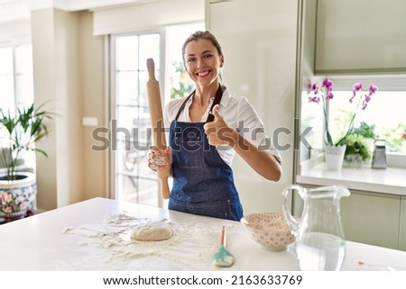 Beautiful blonde woman preparing dough for pizza smiling happy and positive, thumb up doing excellent and approval sign 