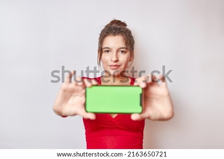 In the photo soft focus. Pretty girl holding a smartphone with a green display. Demonstration of the image on the smartphone screen.