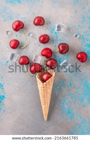 cherry fruit, delicious ripe and fresh cherries and ice cubes popping out of ice cream waffle cone on blue gray background or surface. natural ice cream concept photo with beautiful real fruits