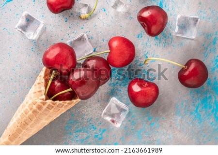 cherry fruit, top view delicious fresh red cherries and ice cubes popping out of ice cream waffle cone on blue gray background or surface. natural ice cream concept photo with beautiful real fruits