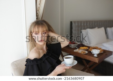 In the photo, the girl is drinking coffee at her balcony. A man takes a picture of her, she is enjoying the morning and breakfast
