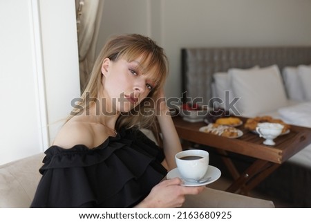 In the photo, the girl is drinking coffee at her balcony. A man takes a picture of her, she is enjoying the morning and breakfast