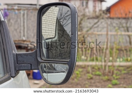 one big black plastic car mirror next to the gray glass of a white auto on the street