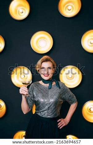 mature stylish elegant woman with glass of sparkling wine on lamps dark background. Party, celebration, anti age concept 