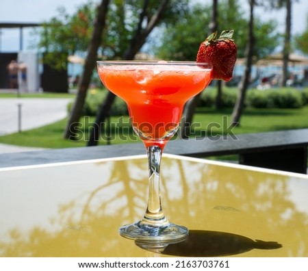 Icy red cocktail decorated with strawberries. A glass of drink on the table, in a cafe, on terrace