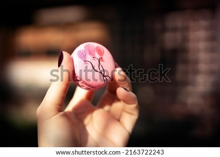 Woman holding a pink macaron sweet with birthday balloons