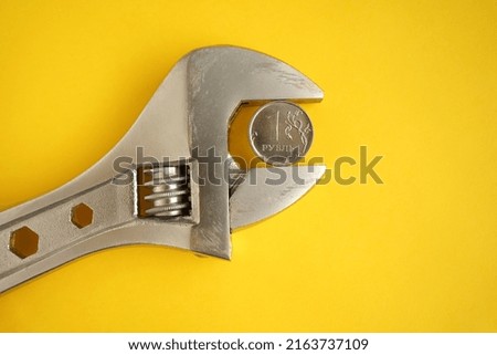         A coin of one Russian ruble is clamped with a wrench on a yellow background. The idea of the collapse of the ruble and economy sanctions against                      