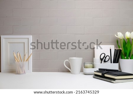 Front view blank picture frame, houseplant, pencil holder, book and coffee cup on white table. Minimal workplace, Copy space for your text.