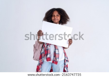 Portrait of a stylish African American teenager girl holding a white horizontal A3 card in her hands on a white background.  Space for text  and mockup.