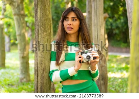 Portrait of a brunette Caucasian girl on vacation in nature taking photos with the camera, wearing a green and white sweater