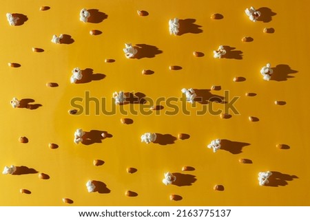 Popcorn and corn kernels are randomly arranged on a yellow background. Hard light and big shadows. Photography for advertising cinemas, cafes, restaurants, coffee houses. Horizontal photo.