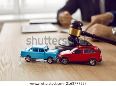 Little crashed autos on table in courtroom. Gavel and two small toy car models on desk in courthouse. Concept of lawyer services, civil court trial, vehicle accident case study, and insurance coverage