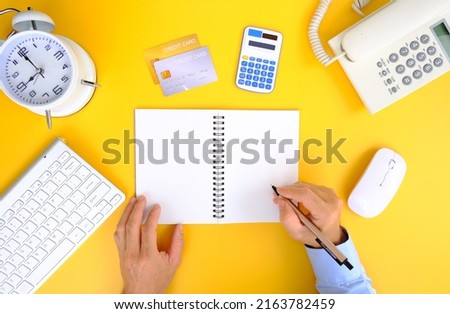 Office desk with smartphone, laptop computer, cup of coffee, and office tools. Flat lay, top view with copy space. A bank notepad and a pen are on top of an office desk table containing computer tools