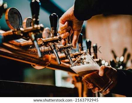 bartender hand at beer tap pouring a draught beer in glass serving in a bar or pub. tap room Royalty-Free Stock Photo #2163792945