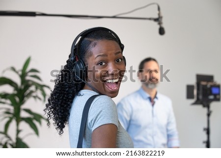 African American Woman Happy Wearing Headphones Working as an Audio Person on a Video Production Set. Interview Subject, Microphone and Lighting in Background