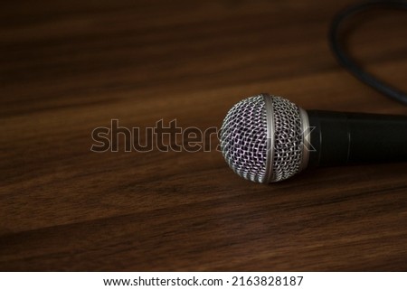 Photo of a dynamic concert microphone Shure sm 58 and wire on a wooden background. Musical vocal equipment for professional performances, lectures, podcasts, stand up and song recording