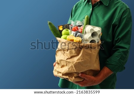 Adult man holding paper grocery bag filled with daily grocery from super market, isolated on blue background, copy space.  Royalty-Free Stock Photo #2163835599