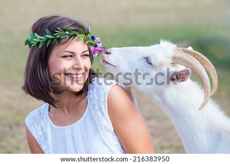 Funny picture a beautiful young girl farmer with a wreath on her head with white goat.
