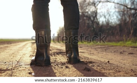 agriculture. man farmer in rubber a boots walk along road near a black field. man farmer worker walk home after harvesting end of sunset the working day feet in rubber boots agriculture Royalty-Free Stock Photo #2163839617