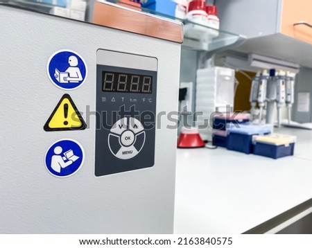 A control panel of a modern laboratory water bath with safety signs. Stickers with pictograms indicates that a user should refer to instruction manual and remain cautious.