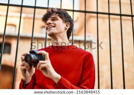 Young hispanic man smiling happy using reflex camera at the city. Royalty-Free Stock Photo #2163848455