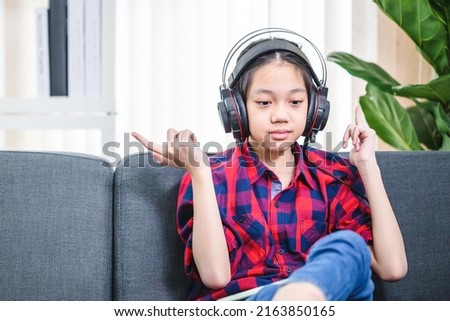 Happy child girl listening to music with digital tablet while sitting on sofa