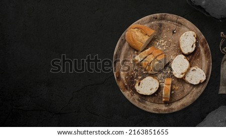 Kitchen table with bread on round wooden chopping board. Presented on the black concrete background with left empty copy space. Table top view.
