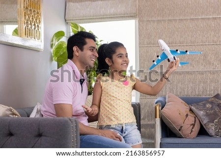 Excited girl and father playing with toy airplane at home