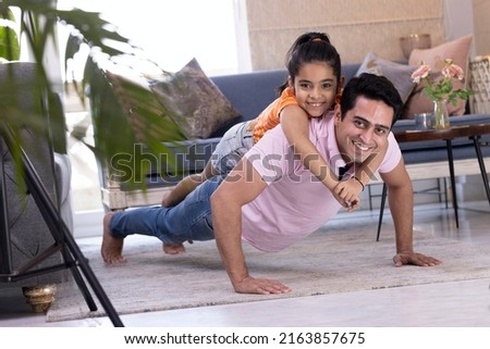 Happy strong father and little daughter enjoying funny activities in living room.