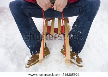Mid adult man sitting on sled in snow, cropped view