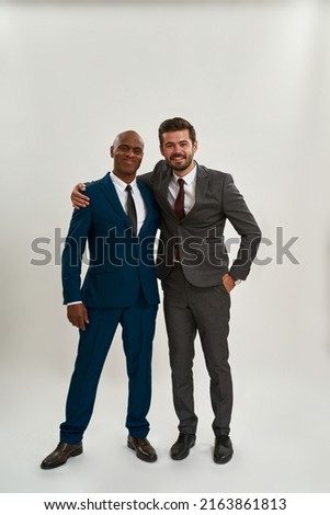 Two pleased multiracial businessmen hugging and looking at camera. Men wearing suits. Modern successful male lifestyle. Teamwork. Isolated on white background. Studio shoot. Copy space Royalty-Free Stock Photo #2163861813