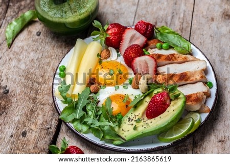 Fried egg, avocado, strawberry, grilled chicken fillet, cheese, nuts and arugula, Low carb high fat breakfast, Ketogenic diet. top view.