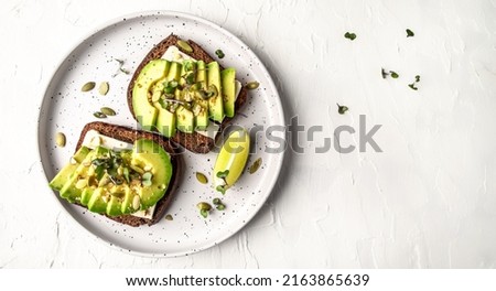 Healthy avocado toasts with rye bread, sliced avocado, cheese, pumpkin, nut and sesame for breakfast or lunch. Vegetarian food. Vegan menu. Long banner format. top view. Royalty-Free Stock Photo #2163865639